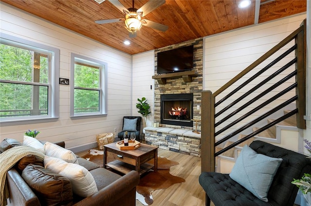 living room featuring ceiling fan, wooden ceiling, a stone fireplace, light hardwood / wood-style flooring, and wood walls