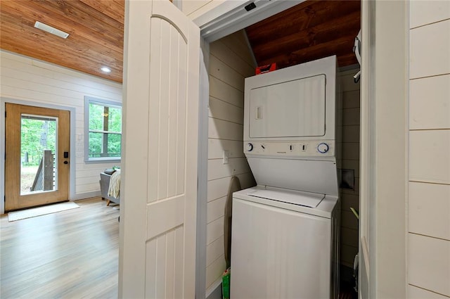 washroom with wood walls, stacked washer and dryer, wood ceiling, and light wood-type flooring