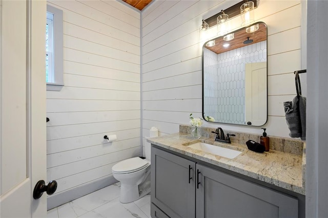 half bathroom featuring toilet, marble finish floor, wood walls, and vanity