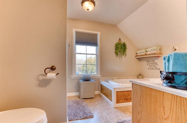 bathroom with tile patterned floors, vanity, vaulted ceiling, tiled tub, and toilet