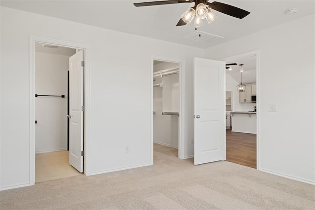 unfurnished bedroom featuring light carpet, a closet, a spacious closet, and ceiling fan