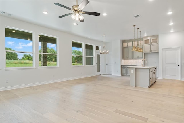 unfurnished living room featuring sink, ceiling fan with notable chandelier, and light wood-type flooring