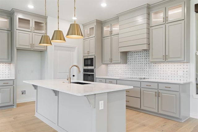 kitchen with light wood-type flooring, an island with sink, stainless steel appliances, and sink