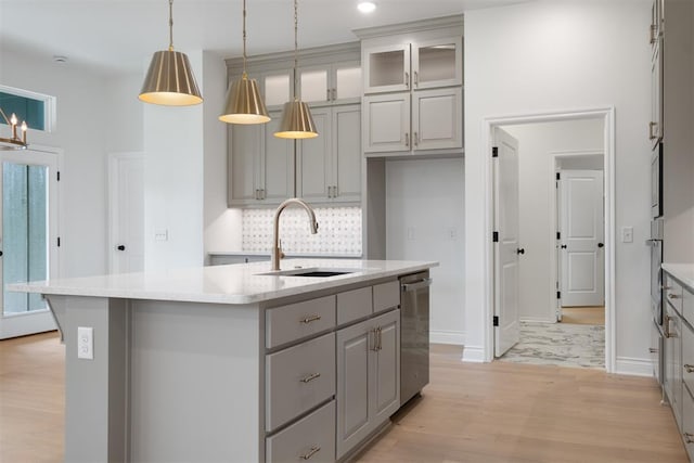 kitchen with gray cabinetry, a center island with sink, sink, decorative light fixtures, and light hardwood / wood-style floors