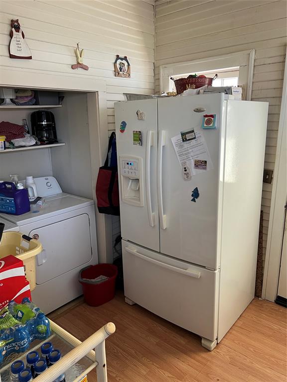 kitchen featuring wood walls, washer / dryer, white refrigerator with ice dispenser, and light wood-type flooring