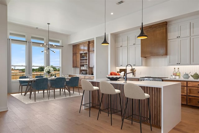 kitchen with white cabinets, a notable chandelier, an island with sink, and hardwood / wood-style flooring