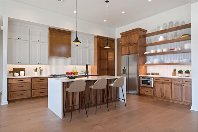 kitchen with appliances with stainless steel finishes, light hardwood / wood-style flooring, white cabinets, hanging light fixtures, and a breakfast bar area