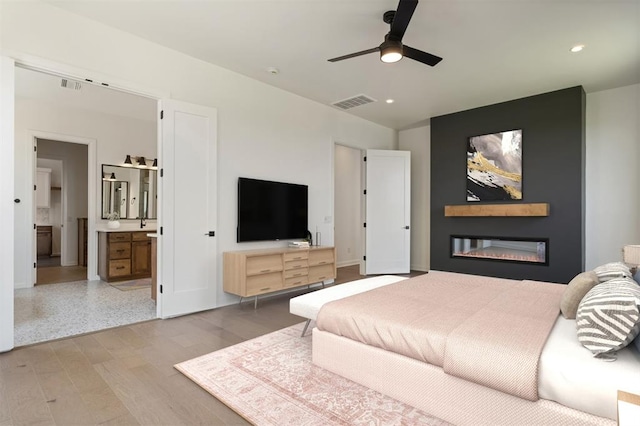 bedroom featuring ceiling fan, ensuite bathroom, and light hardwood / wood-style flooring