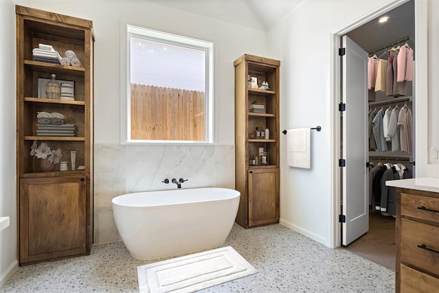 bathroom featuring vanity, a bathtub, lofted ceiling, and tile walls