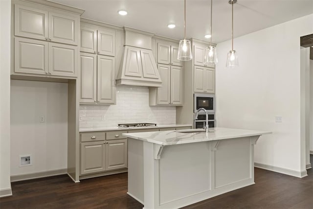 kitchen with a kitchen island with sink, dark hardwood / wood-style floors, light stone countertops, custom range hood, and stainless steel appliances