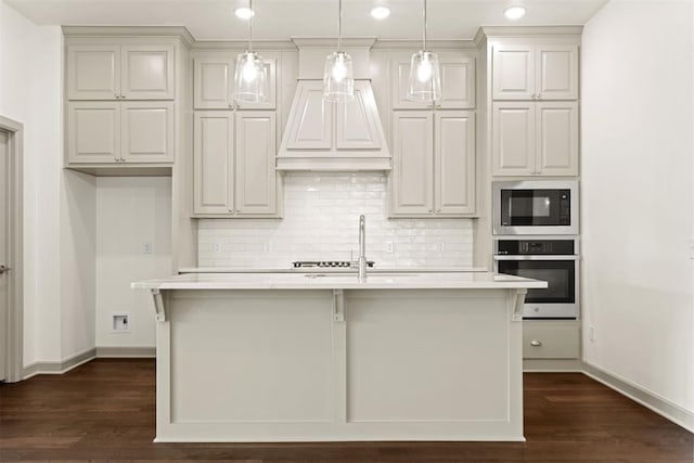 kitchen featuring decorative light fixtures, oven, built in microwave, and a kitchen island with sink