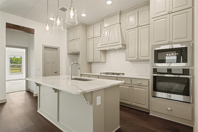 kitchen featuring pendant lighting, a kitchen island with sink, sink, appliances with stainless steel finishes, and light stone counters