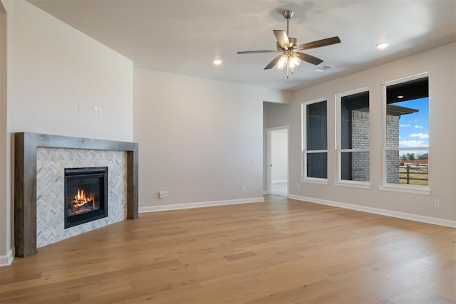 unfurnished living room featuring a tile fireplace, ceiling fan, and light wood-type flooring