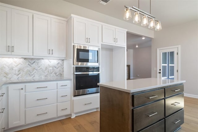 kitchen with pendant lighting, stainless steel appliances, white cabinetry, and light hardwood / wood-style flooring