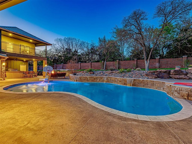 pool at dusk with a patio area, pool water feature, exterior bar, and a hot tub