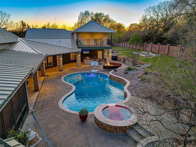 pool at dusk with an in ground hot tub and a patio area