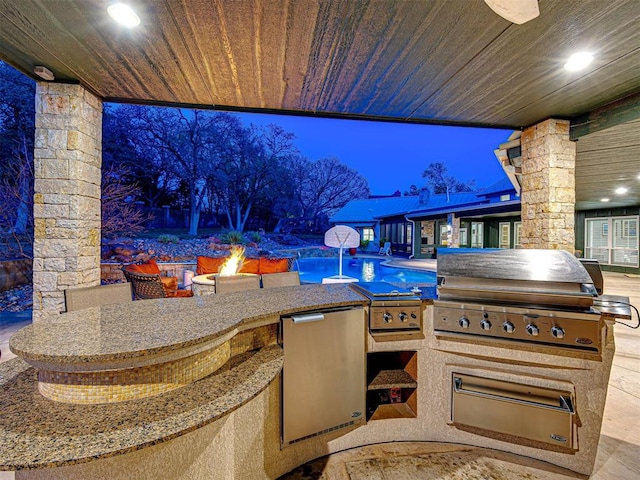 view of patio with grilling area, a swimming pool, exterior kitchen, and a fire pit