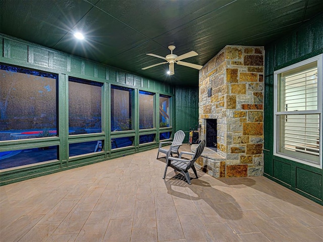 sunroom featuring ceiling fan and a fireplace