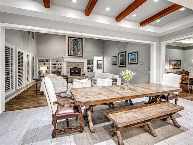 dining space featuring beamed ceiling, light wood-type flooring, and a stone fireplace