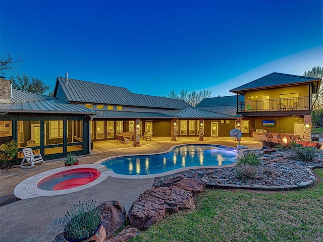 pool at dusk with an in ground hot tub and a patio