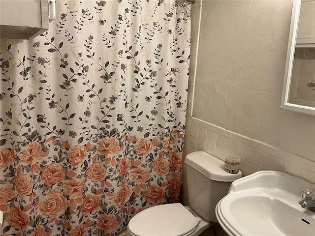 bathroom featuring toilet, sink, walk in shower, and tile walls