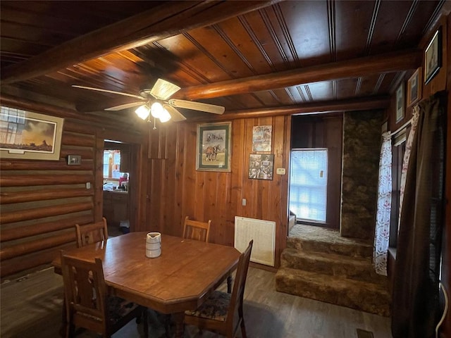 dining room featuring wooden ceiling, dark wood-type flooring, ceiling fan, rustic walls, and beam ceiling