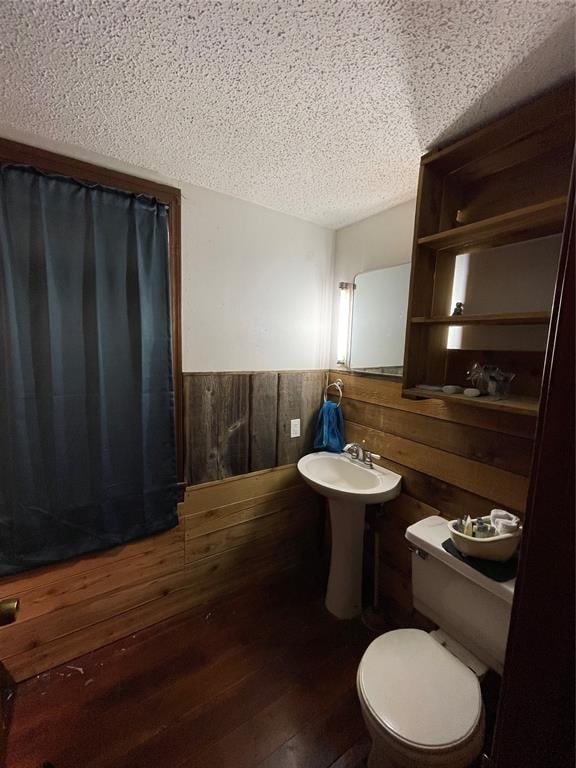 bathroom featuring wood walls, sink, toilet, a textured ceiling, and wood-type flooring