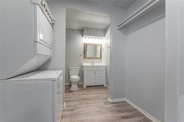 bathroom with wood-type flooring, a textured ceiling, stacked washer / drying machine, toilet, and vanity