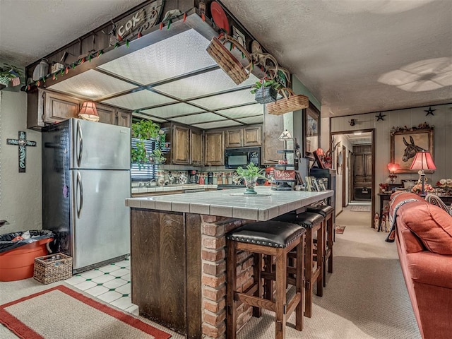 kitchen featuring stainless steel refrigerator, tile countertops, light carpet, and a breakfast bar area