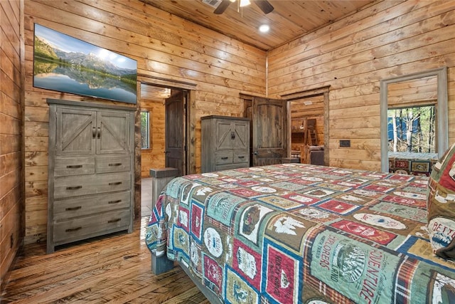 bedroom featuring multiple windows, hardwood / wood-style floors, ceiling fan, and wooden walls