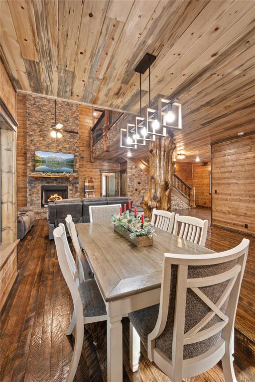 dining space featuring log walls, wooden ceiling, dark wood-type flooring, a stone fireplace, and wooden walls