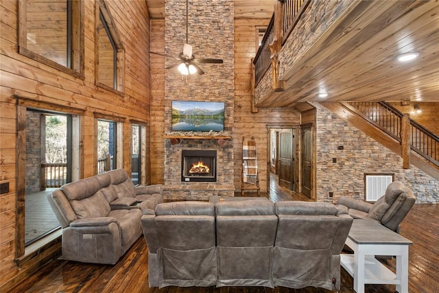 living room with wood walls, dark wood-type flooring, ceiling fan, a towering ceiling, and a fireplace