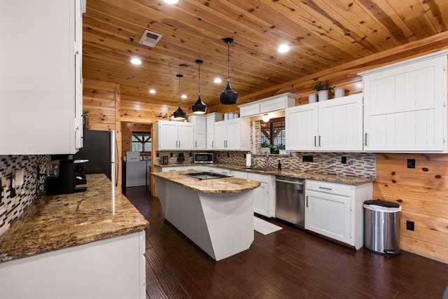 kitchen featuring pendant lighting, wood walls, a center island, white cabinetry, and stainless steel appliances