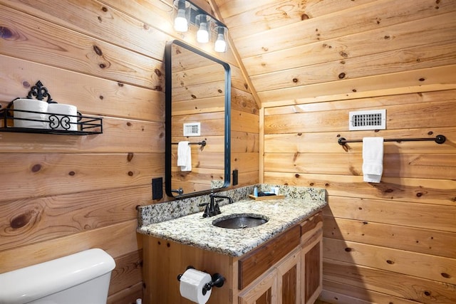 bathroom with vanity, toilet, wooden walls, and vaulted ceiling