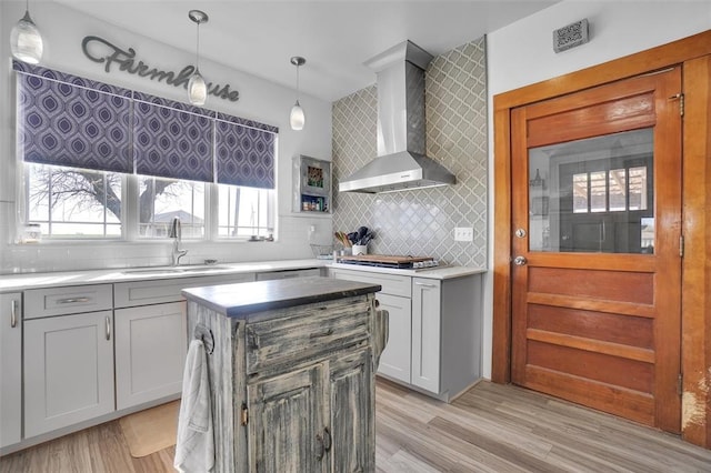 kitchen with a center island, sink, wall chimney exhaust hood, and decorative light fixtures