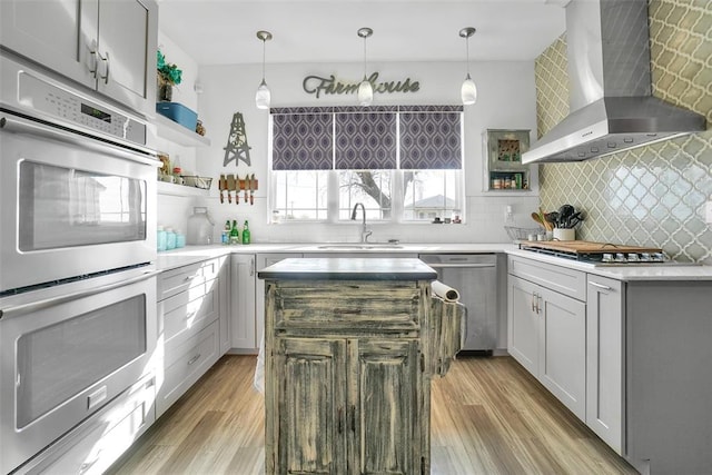 kitchen featuring a center island, wall chimney exhaust hood, gray cabinets, decorative backsplash, and stainless steel appliances