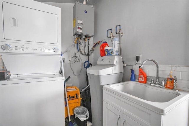 laundry area featuring stacked washer / dryer, tankless water heater, sink, and cabinets