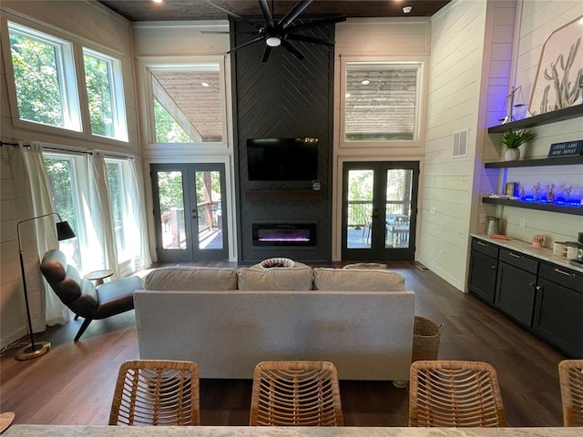 living room with a high ceiling, french doors, wooden walls, ceiling fan, and dark hardwood / wood-style flooring