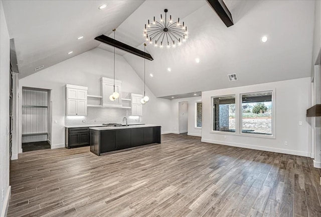 kitchen with white cabinets, an island with sink, beamed ceiling, decorative light fixtures, and wood-type flooring