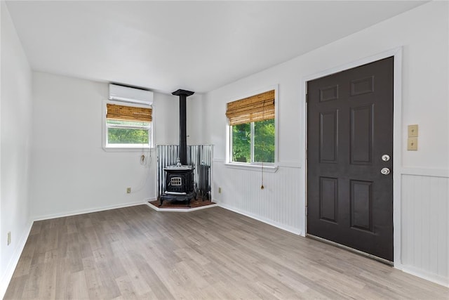 unfurnished living room featuring an AC wall unit, a wood stove, plenty of natural light, and light hardwood / wood-style floors