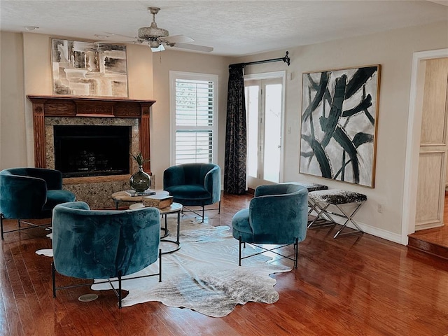 living area with hardwood / wood-style floors, ceiling fan, a textured ceiling, and a high end fireplace