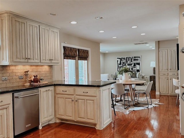 kitchen featuring kitchen peninsula, backsplash, stainless steel dishwasher, dark stone counters, and hardwood / wood-style floors