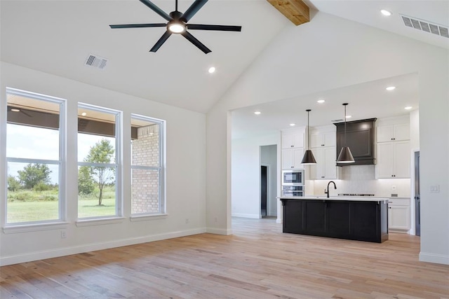 kitchen with white cabinetry, light hardwood / wood-style flooring, an island with sink, and pendant lighting