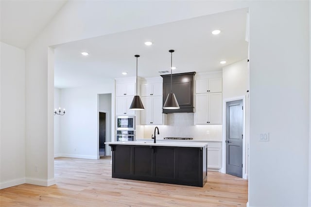 kitchen with decorative light fixtures, light hardwood / wood-style floors, white cabinetry, and an island with sink