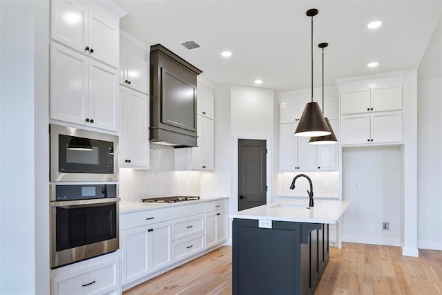 kitchen with a center island with sink, sink, light wood-type flooring, white cabinetry, and stainless steel appliances