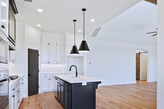 kitchen featuring sink, a barn door, a center island with sink, white cabinetry, and hanging light fixtures