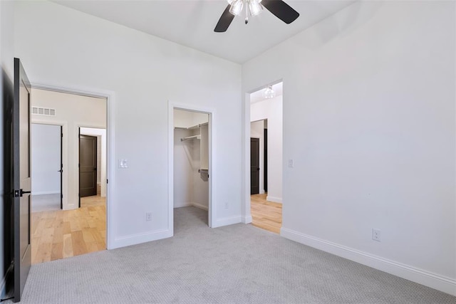 unfurnished bedroom featuring a closet, a spacious closet, ceiling fan, and light colored carpet