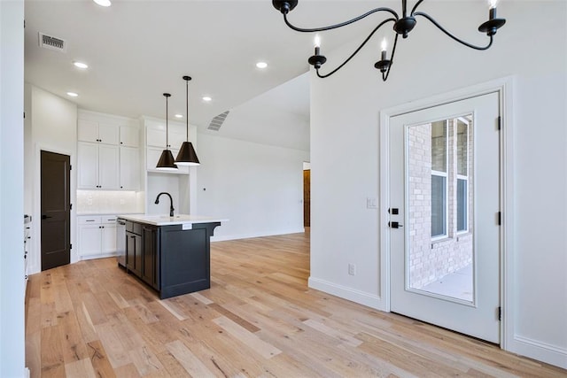 kitchen with white cabinetry, an island with sink, pendant lighting, and light hardwood / wood-style floors