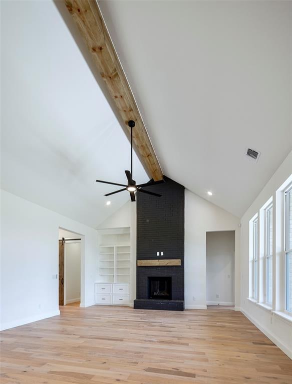 unfurnished living room featuring lofted ceiling with beams, ceiling fan, light wood-type flooring, a fireplace, and built in features