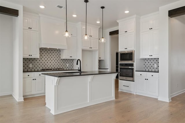 kitchen featuring white cabinets, a kitchen island with sink, sink, and appliances with stainless steel finishes